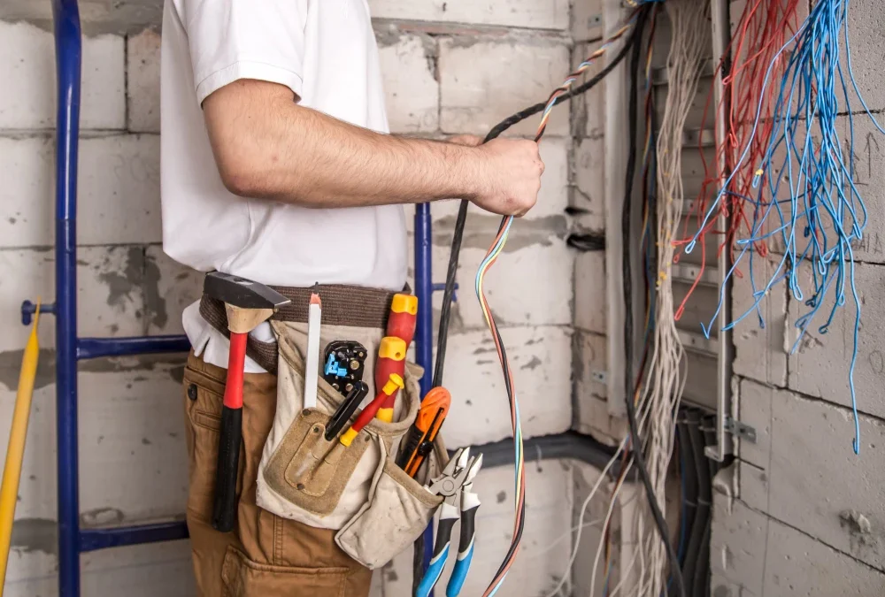 Alet kemerinde çekiç, tornavida ve pense taşıyan elektrikçinin soyulmuş çok damarlı kabloyu tutan eli