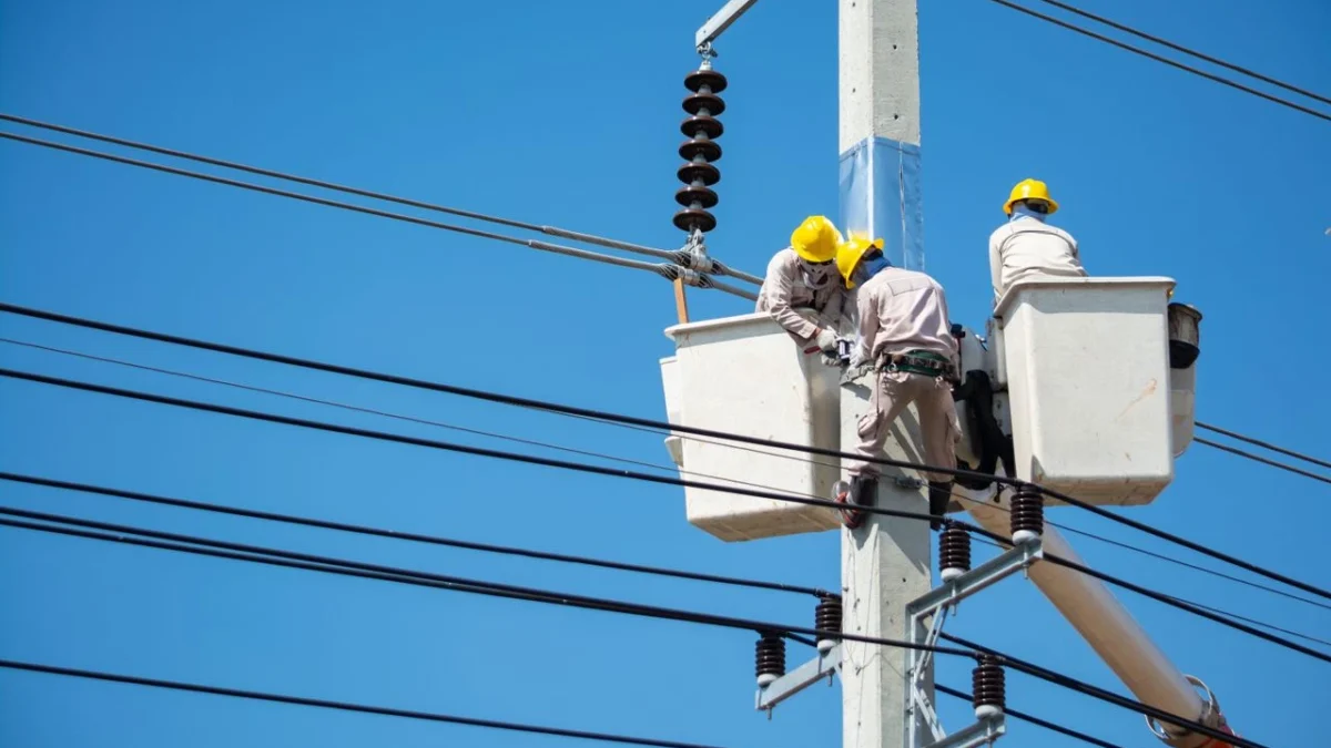 Mavi gökyüzüne karşı beton enerji direğinde sepetli araç platformlarından hat bakımı yapan üç kişilik ekip